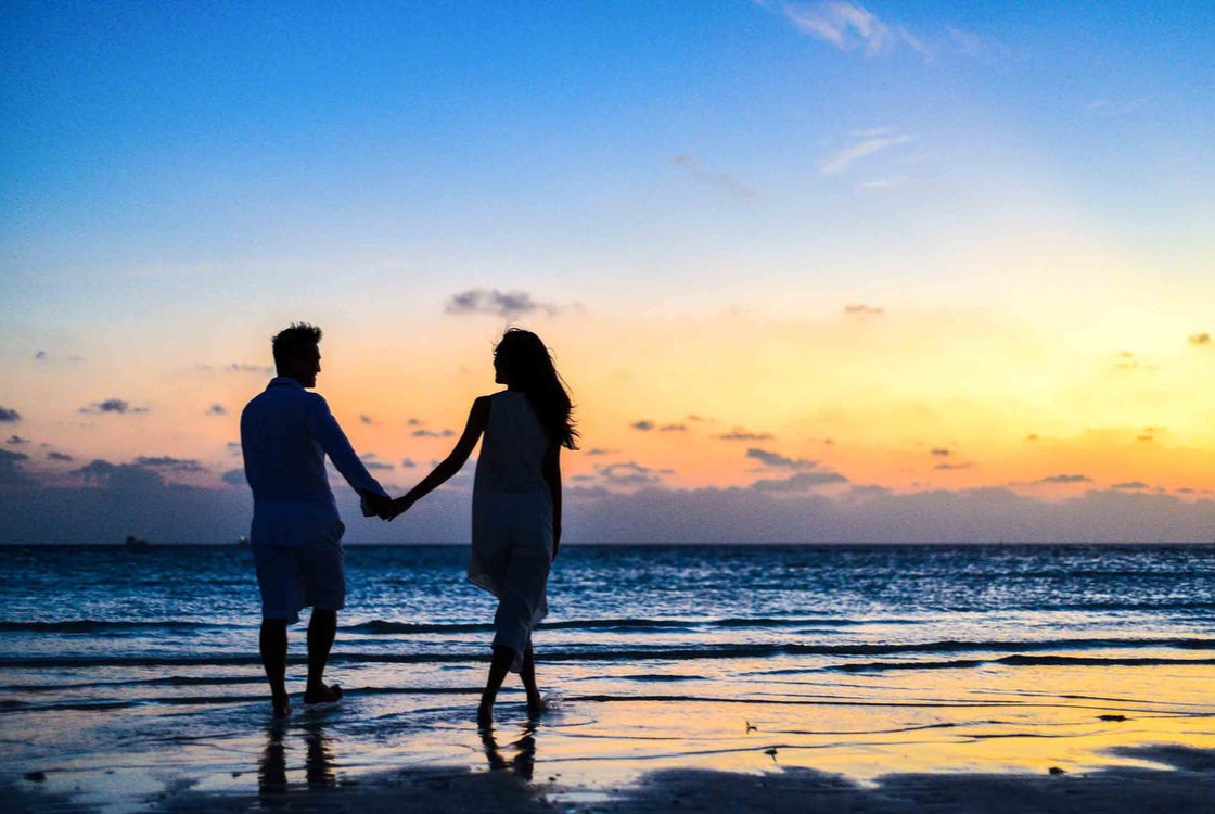 kobieta i mężczyzna trzymający się za rękę na tle zachodzącego słońca nad morzem